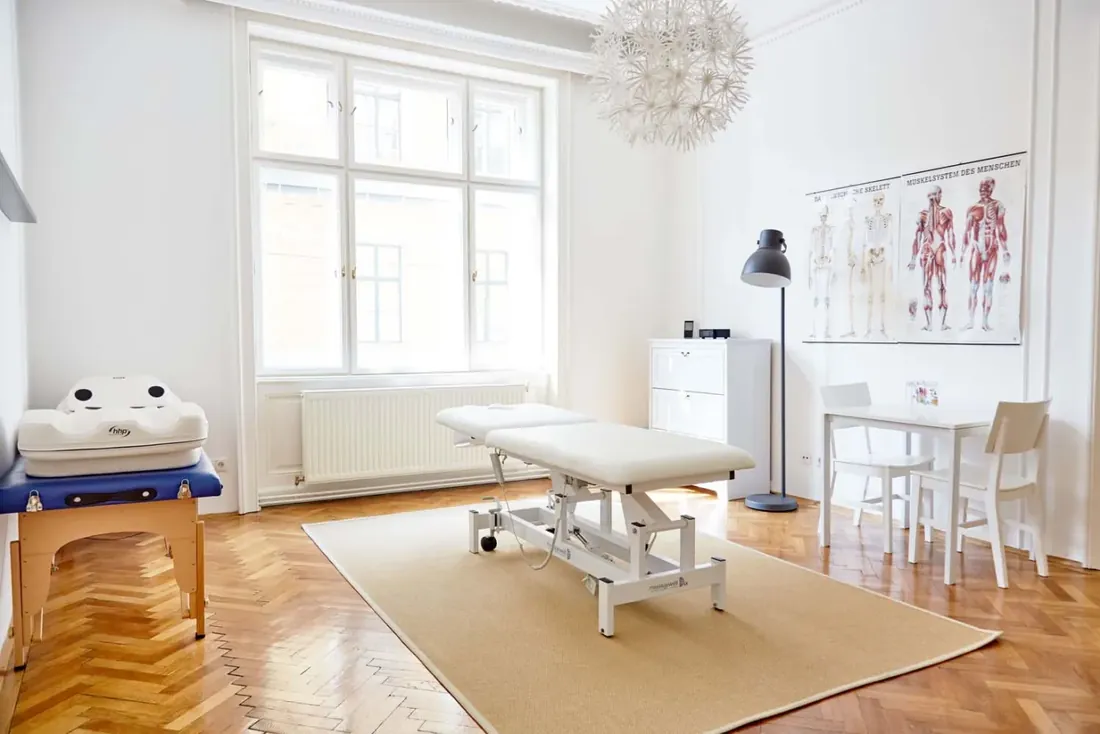 Heller Behandlungsraum mit Liege und Anatomie-Tafeln